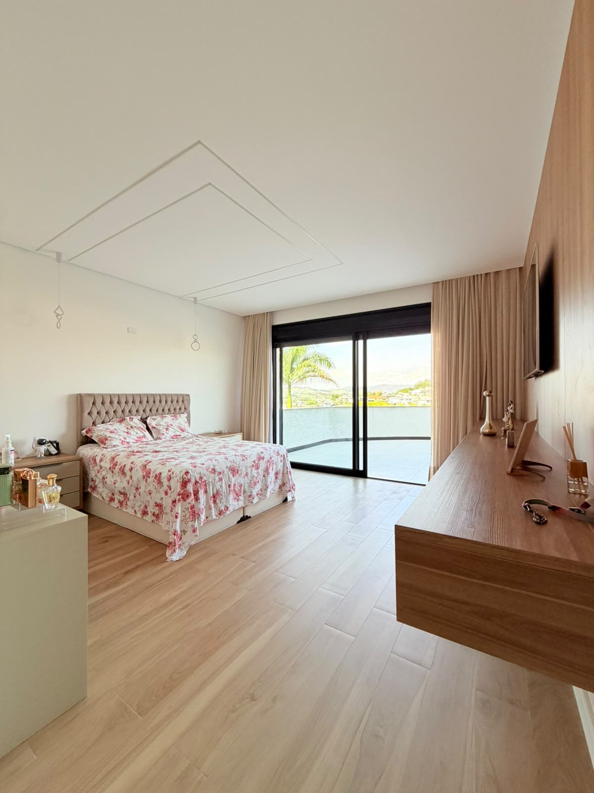 Suíte principal com cama, piso de madeira e porta de vidro para a varanda